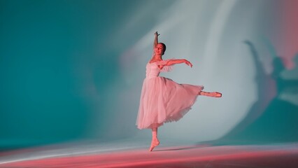 Portrait of female on green background in pink neon light studio. Young ballerina in white tulle showing beautiful element of choreography. © kinomaster