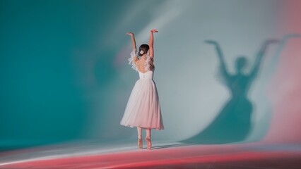 Portrait of female on green background in pink neon light studio. Young ballerina in white tulle showing beautiful element of choreography. © kinomaster