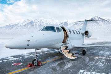 Modern white business jet with an opened gangway door at the winter airport apron on the background...