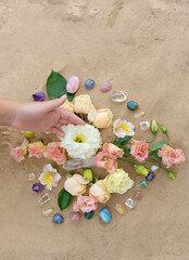 Fototapeta na wymiar Hand with gemstones and flowers for Crystal Ritual on sand background. Esoteric spiritual wiccan practice for relaation, harmony, life balance. spa concept. Flower Mandala with crystals. top view