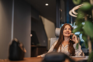Confident woman having phone call with client during phone call while working alone at modern...