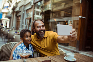 Fototapeta na wymiar Stepfather taking selfie with child son at city cafe