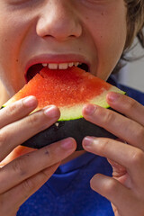 happy boy holding a triangular slice of watermelon in his hands with his mouth open