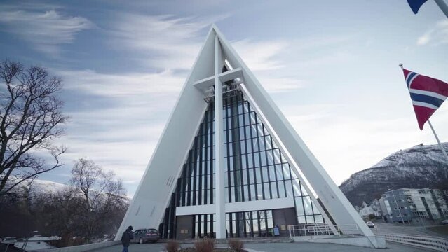 arctic cathedral in tromso with waving norwegian flag and a man approaching to church during winter morning
