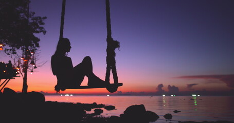 Woman silhouette relax swinging on sway against bright sea sunset sky. Outdoor lifestyle travel on summer holiday vacation, exotic island landscape. Colorful bokeh unfocused light.