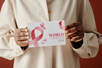 Hands of unrecognizable African American woman in white shirt holding breast cancer postcard with pink ribbon in front of camera