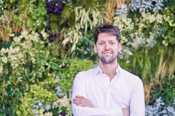 portrait of a man dressed in a white shirt against a background of a vertical garden.