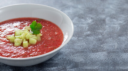 Gazpacho soup garnished with cucumber and cilantro, in white bowl, horizontal, copy space