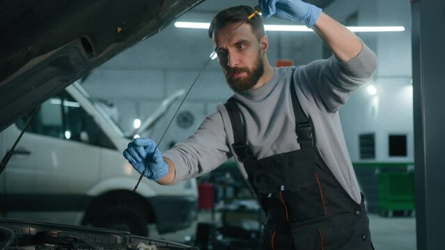 Caucasian 30s man opening car hood in repair workshop check engine oil level at auto service male mechanic maintenance engineer repairing automobile in garage using dipstick tool checking fuel vehicle