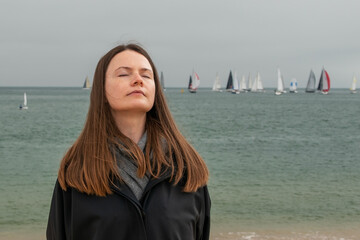 Young woman on the beach with a view of the sea and sailing boats
