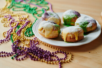 Group of appetizing doughnuts sprinkled with sugar powder on plate standing on table in front of camera among colorful beads