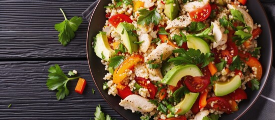 Chicken and vegetable couscous salad with tomatoes, avocado, bell pepper, parsley, and lemon juice, served on a black table surface in a close-up shot.