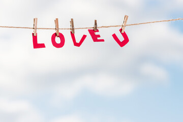 Red letters of love you hanging on a rope with clothespins on a background of cloudy sky.