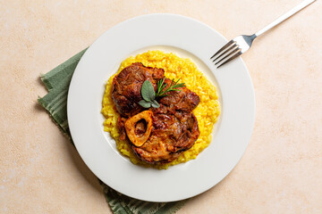 Top view of plate with Italian dish Ossobuco, braised beef meat with bone served with saffron risotto alla milanese, specialty of Lombard cuisine. Beige background.