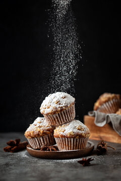Homemade cinnamon muffins with streusel sprinkled with powdered sugar on black background.