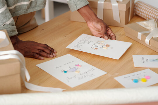 Unrecognizable African American girl holding greeting postcard for Mother day with drawings while preparing gift for mom