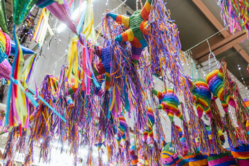 Colorful piñatas of different shapes and sizes hanging over the stalls of a traditional Mexican...