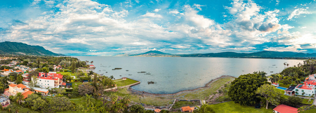 A panorama of mountains and lake with the sunset as background. Clouds and blue sky with trees and colors