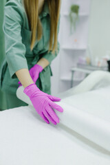 An hair removal master spreads a protective film on the couch for a girl patient before starting a procedure in a beauty salon, a cosmetologist in a cosmetology office loves sterility and cleanliness
