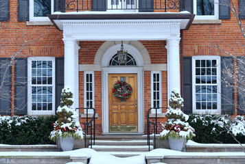 House in winter with elegant wood grain front door with Christmas wreath