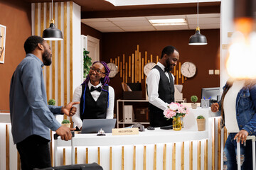 Pleasant conversation between receptionist and customer in hotel. Friendly smiling young African American woman front desk agent greeting guest at reception counter helping with check-in process