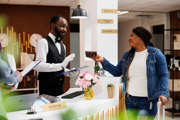 Young African American woman tourist showing passport to hotel staff during check-in process at...