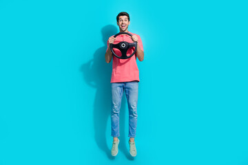 Full length photo of excited funky man wear pink t-shirt jumping high riding automobile isolated blue color background