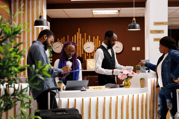 Young African American couple filling up registration form while checking in at hotel front desk....