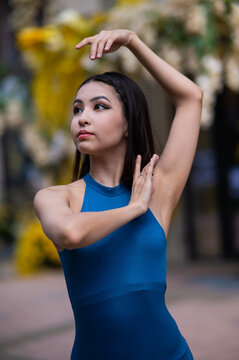 Close-up portrait of a beautiful Asian ballerina posing against the background of a building decorated with flowers. Vertical photo. 