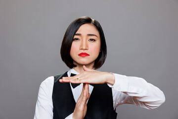 Restaurant serious asian waitress dressed in uniform showing timeout symbol with palms portrait....
