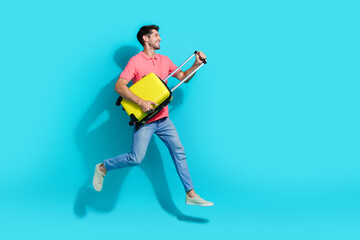 Fototapeta na wymiar Full length photo of funky excited man wear pink t-shirt jumping high holding baggage looking empty space isolated blue color background