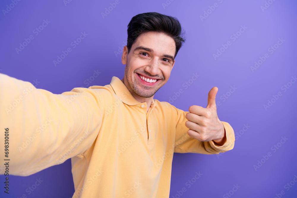 Sticker Photo of good mood charming guy wear yellow polo showing thumb up recording video vlog isolated violet color background