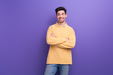Photo of dreamy positive man dressed yellow shirt arms folded looking empty space isolated purple...