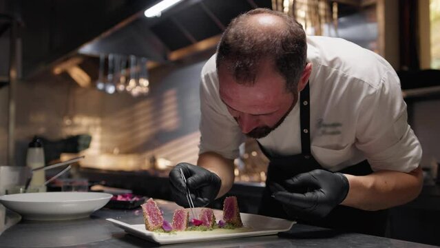 Chef is plating breaded tuna fish fillets in kitchen of restaurant