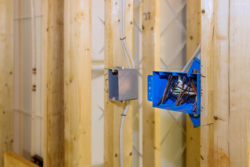 Located on wall above wooden frame beam is plastic electrical switch box with wires