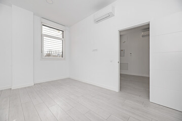 An empty room in an apartment with white walls, light wooden floors, air conditioning high on the wall