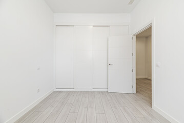 An empty room with built-in wardrobes with white sliding doors along one wall