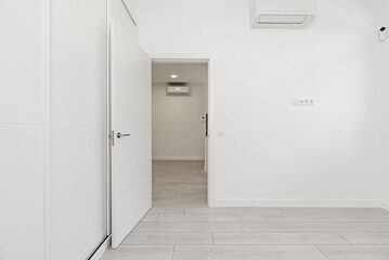 A room in an empty loft-style home with built-in wardrobes with white sliding doors