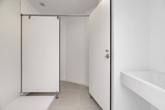 A bathroom with a white-walled shower cubicle with an industrial-style screen and a white porcelain sink in the corner