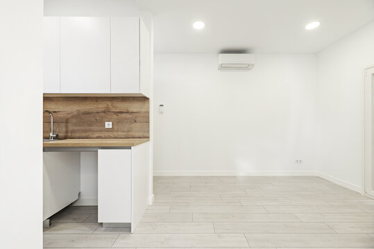 Image of a newly installed small kitchen with white furniture with backsplash and countertop of the same material in a loft-style apartment