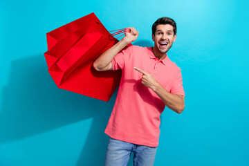 Portrait of young excited brunet hair guy wearing pink t shirt direct finger his shopping packages...