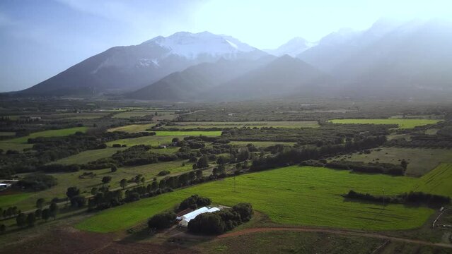 Drone footage of green fields with mountains under dusk sky in the background in Tithorea, Greece