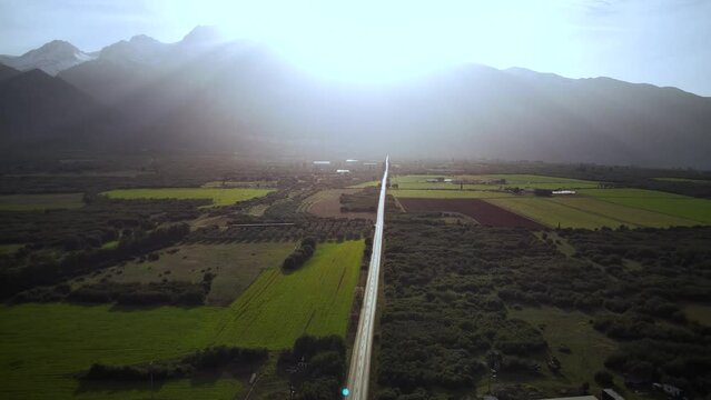 Aerial footage of a road passing through cultivated green fields at sunset in Tithorea, Greece