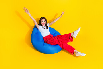 Top view full length photo of excited carefree woman dressed t-shirt sitting bean bag rising arms...