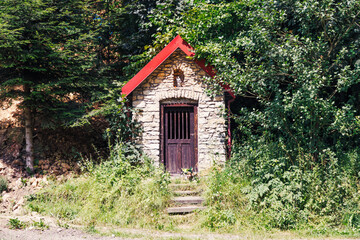 Fototapeta na wymiar A small chapel in a summer forest among greenery.