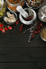 Mortar with pestle and many different herbs on wooden table, flat lay. Space for text