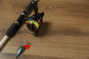 Fishing rod with spinning reel and bait on wooden background, closeup. Space for text