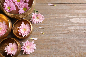 Tibetan singing bowls with water and beautiful flowers on wooden table, flat lay. Space for text