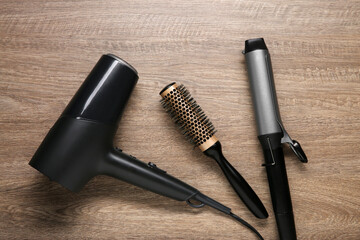 Curling iron, round brush and hair dryer on wooden background, flat lay