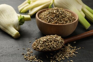 Fresh fennel bulbs, bowl and spoon with seeds on gray table, closeup